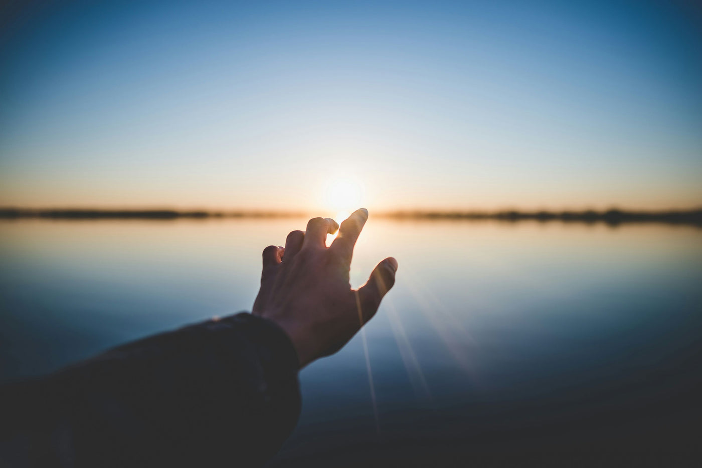 first-person view of hand reaching toward sunrise over water, symbolizing wellness journey and recovery tools