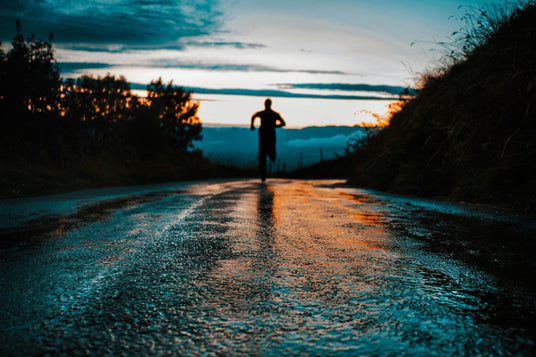 man running toward sunrise on wet road, symbolizing peak performance through wellness routines and athletic recovery